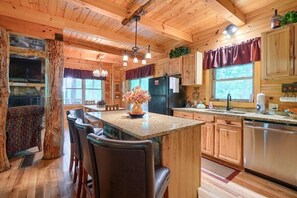 A rustic cabin-style kitchen with wooden cabinets, a granite island, and a stone fireplace.