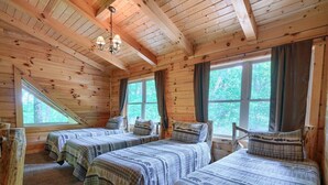 Eine Holzhütte mit drei Betten, einer geneigten Decke und großen Fenstern.