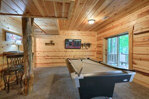 Una mesa de billar en una habitación de madera con un banco y una mesa con una lámpara.