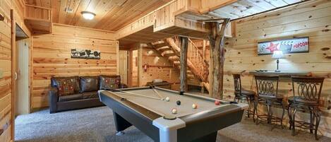 Un interior de madera con mesa de billar, sofá y zona de bar.