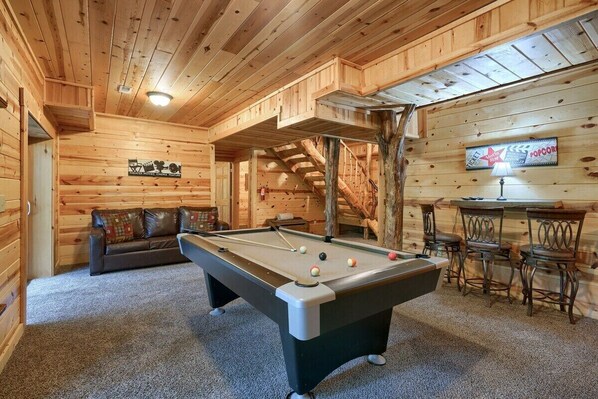 Un interior de madera con mesa de billar, sofá y zona de bar.