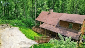A log cabin with a porch, surrounded by dense forest.