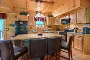 Interior de una cabaña de madera con cocina, que incluye un refrigerador, estufa y mesa de comedor con sillas.
