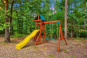Un parque infantil con tobogán y columpios en un área boscosa.