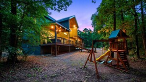 A lodge with a wooden exterior, a covered deck, and a play area with a slide.
