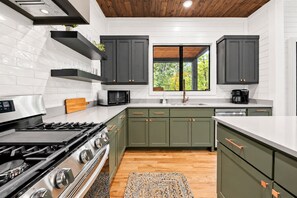 Una cocina moderna con estufa a gas, microondas y ventana con vista a árboles.