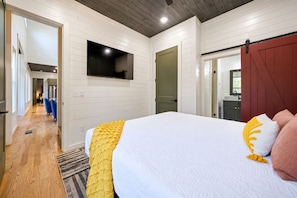 A bedroom with a large bed, a television mounted on the wall, and a wooden floor.