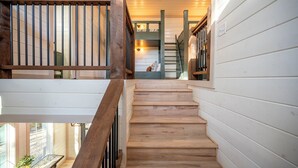 A wooden staircase with a railing, leading to a room with a bed and a window. - Play & Stay | 4BR Playset, Pool/Ping Pong, Arcade (Broken Bow)