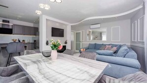 A modern living room with a marble coffee table, a blue sofa, and a dining area with a marble table. - Holiday apartment with balcony (Crikvenica)