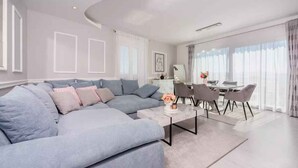 A modern living room with a grey sectional sofa, a coffee table, and a dining area with chairs and a table. - Holiday apartment with balcony (Crikvenica)