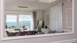 A modern living room with a large window, a dining area with a table and chairs, and a view of the sea. - Holiday apartment with balcony (Crikvenica)