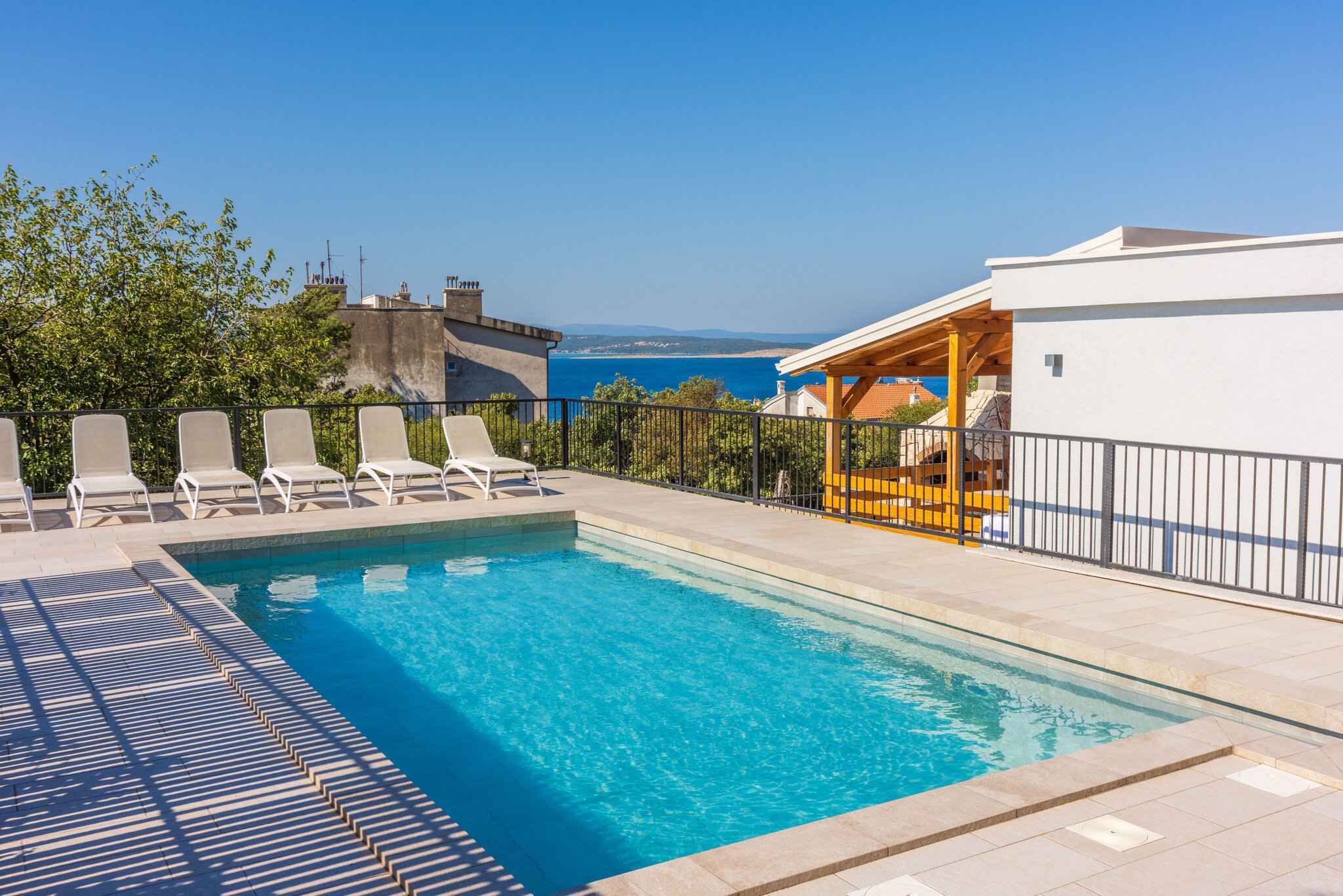 Piscina com espreguiçadeiras, área coberta e vista para o mar.