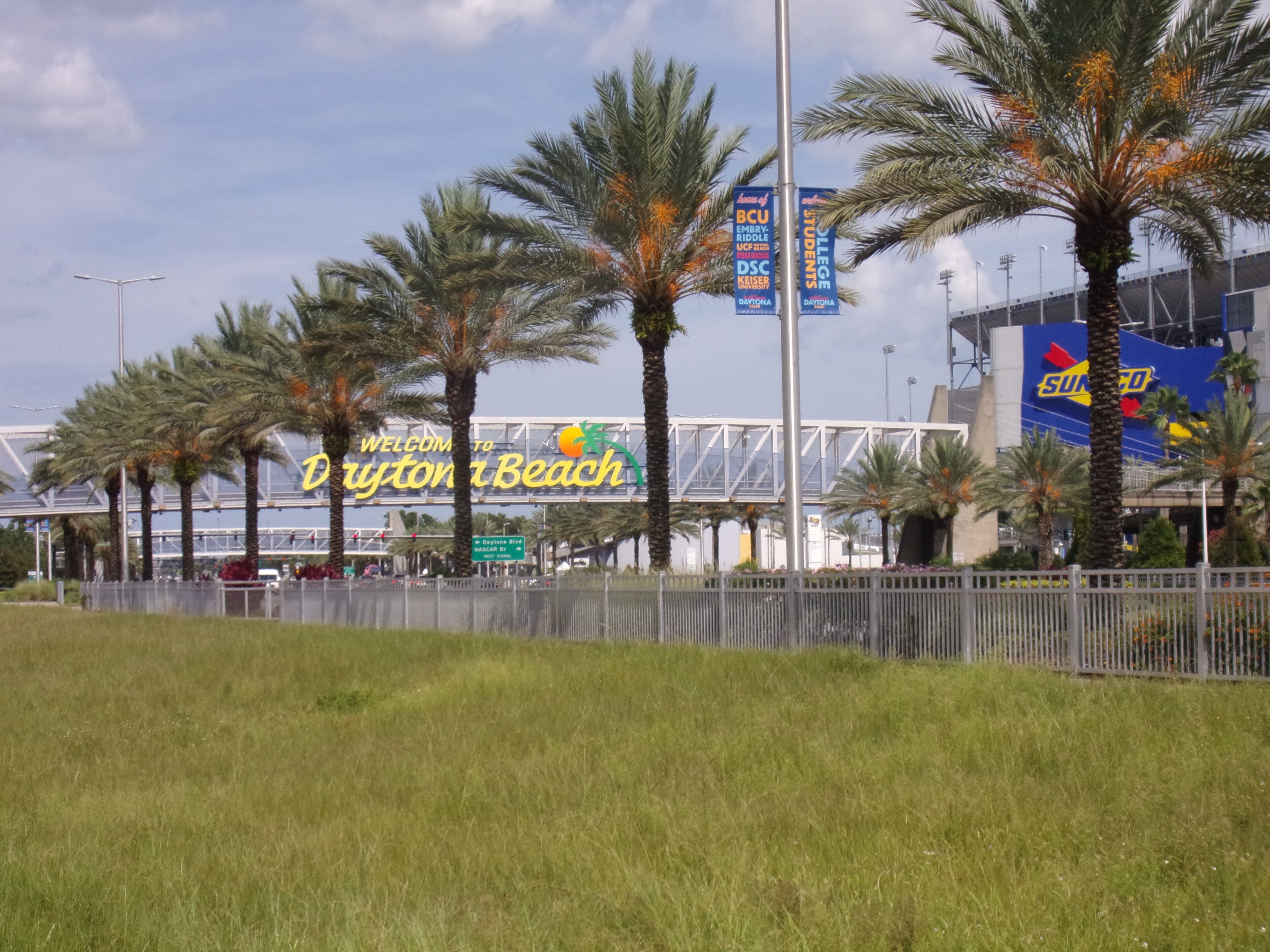 Un panneau de signalisation indiquant l’entrée de Daytona Beach, avec des palmiers et un pont en arrière-plan.