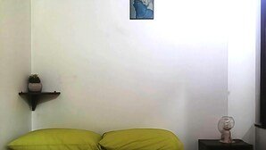 Un lit avec des oreillers verts, une petite étagère avec une plante et un verre posé sur une table de chevet.
