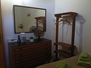Ein Zimmer mit einem Schminktisch, einem Spiegel, einem Ventilator und einem Wäscheständer aus Holz.