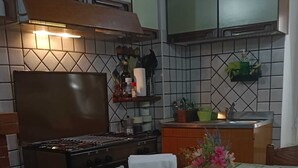 Un coin repas avec une table dressée pour deux personnes, une cuisine en arrière-plan et un mur recouvert de carreaux.
