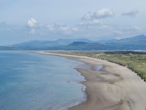 Eine Küstenlandschaft mit einem weiten Sandstrand, sanften Wellen und fernen Bergen unter klarem Himmel.