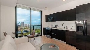 A modern kitchen with a large window, a dining area with a white sofa, and a view of the cityscape. - Lux Studio with Bay Views #3104 (Miami)
