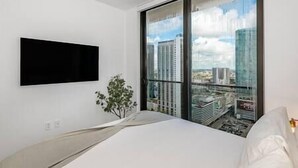A modern bedroom with a large window, a flat-screen TV mounted on the wall, and a neatly made bed. - Luxury 3 BD Condo at The Biscayne Bay #2701 (Miami)