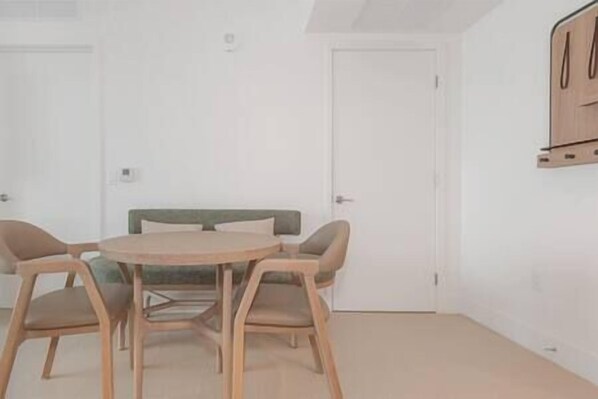 A room with a round table and four chairs, a sofa, and a wooden cabinet.