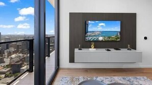 Un salon moderne avec un grand téléviseur fixé au mur, une console au design épuré et un balcon offrant une vue sur la ville.