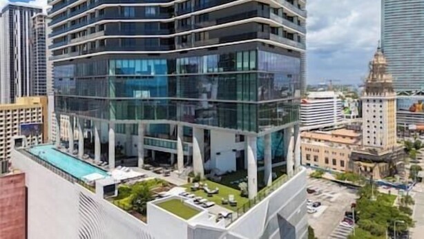 Un hôtel moderne, de grande hauteur, doté d’une façade en verre, de nombreux balcons et d’un espace piscine sur le toit.