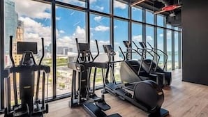 Uma academia com aparelhos de cardio e amplas janelas com vista para a cidade.