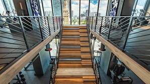A modern staircase with wooden steps and metal railings, leading to an upper floor with gym equipment and a city view. - Classy 3BD in Downtown Miami - #2618 (Miami)