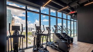 A modern gym with large windows offering a city view, equipped with various cardio machines and dumbbells. - Classy 3BD in Downtown Miami - #2618 (Miami)