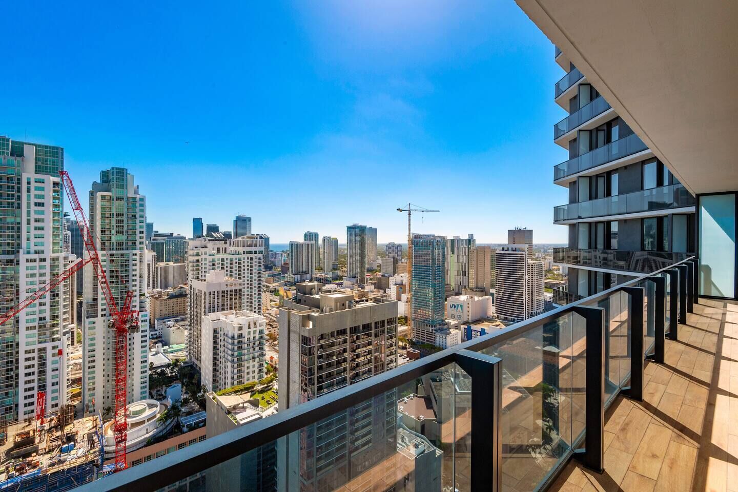 A high-rise building with a modern glass facade, a balcony with a metal railing, and a cityscape view in the background.