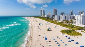 Una playa con una hilera de edificios hoteleros, cielo azul despejado y océano turquesa.