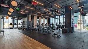 Un gimnasio moderno con equipo de ejercicio, ventanas amplias y vistas a la ciudad.