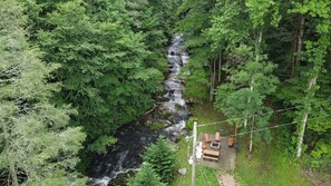 A forested area with a small cabin and a wooden deck overlooking a stream. - Mtn Cabin with Creek Views and Waterfall (Cosby)