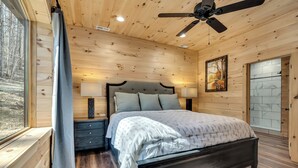 A wooden-paneled bedroom with a bed, nightstands, and a ceiling fan. - Mtn Cabin with Creek Views and Waterfall (Cosby)