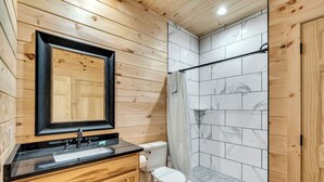 A wooden-paneled bathroom with a sink, toilet, and shower. - Mtn Cabin with Creek Views and Waterfall (Cosby)