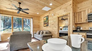 A cozy cabin interior with a sofa, a dining table with a white mug, and a ceiling fan. - Mtn Cabin with Creek Views and Waterfall (Cosby)