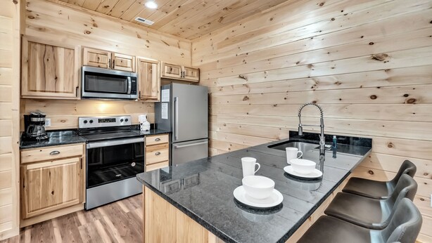 A modern kitchen with wooden walls, stainless steel appliances, and a central island with seating. - Mtn Cabin with Creek Views and Waterfall (Cosby)