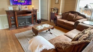 Una sala de estar acogedora con chimenea, un televisor montado encima y un rincón de descanso cómodo con sofá y mesa de centro.