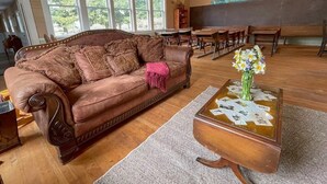 Un salón acogedor con un sofá de cuero marrón, una mesa de centro de madera con un florero, y un ventanal con vistas a árboles.