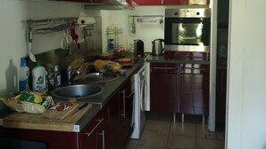 Une cuisine compacte avec des meubles rouges, un évier en acier inoxydable, un four encastré et un four à micro-ondes.
