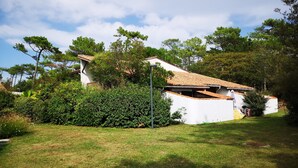 Un bâtiment blanc, doté d’un toit en tuiles, entouré de verdure et d’arbres.