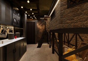 A narrow hallway with a stone wall, a wooden staircase, and a kitchen area with a counter and cabinets.