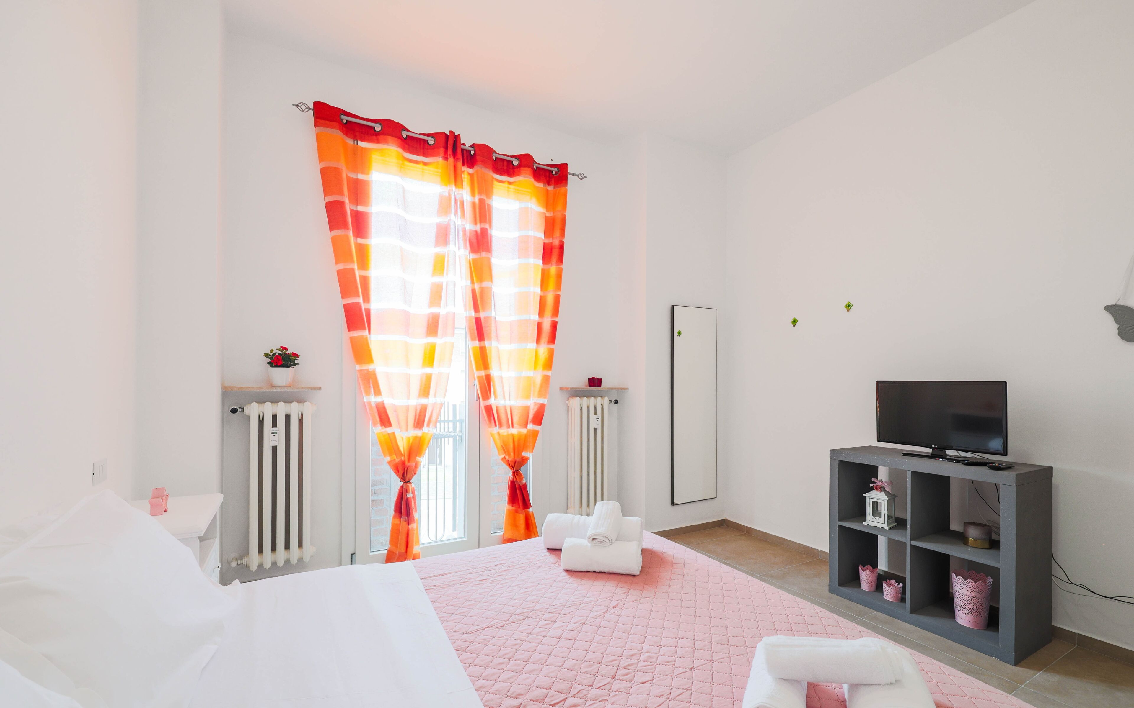 Ein modernes Schlafzimmer mit Bett, Fernseher, Heizkörper und einem Fenster mit Vorhängen.