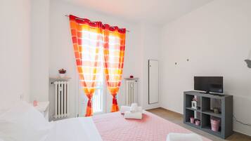 Ein modernes Schlafzimmer mit Bett, Fernseher, Heizkörper und einem Fenster mit Vorhängen.