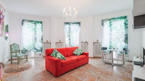 A spacious living room with a red sofa, a chandelier, and tropical-themed curtains. - The prestigious corner of Forli (Forlì)