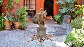 A courtyard with a stone statue, potted plants, and a dog sitting near a door. - Casa de la Cuesta Bed and Breakfast (San Miguel de Allende)