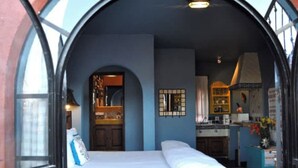 A bedroom with a bed, a window, and a view of a kitchen and dining area. - Casa de la Cuesta Bed and Breakfast (San Miguel de Allende)