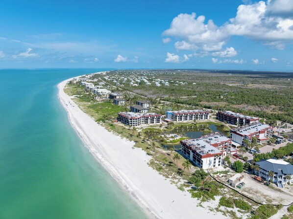 Vista aérea de un complejo turístico costero con villas frente a la playa, un puerto deportivo y un campo de golf.