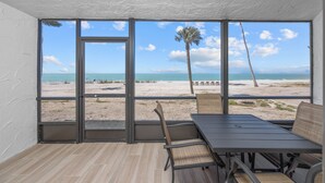 Une pièce dotée d’une grande fenêtre donnant sur une plage, d’une table et de deux chaises.