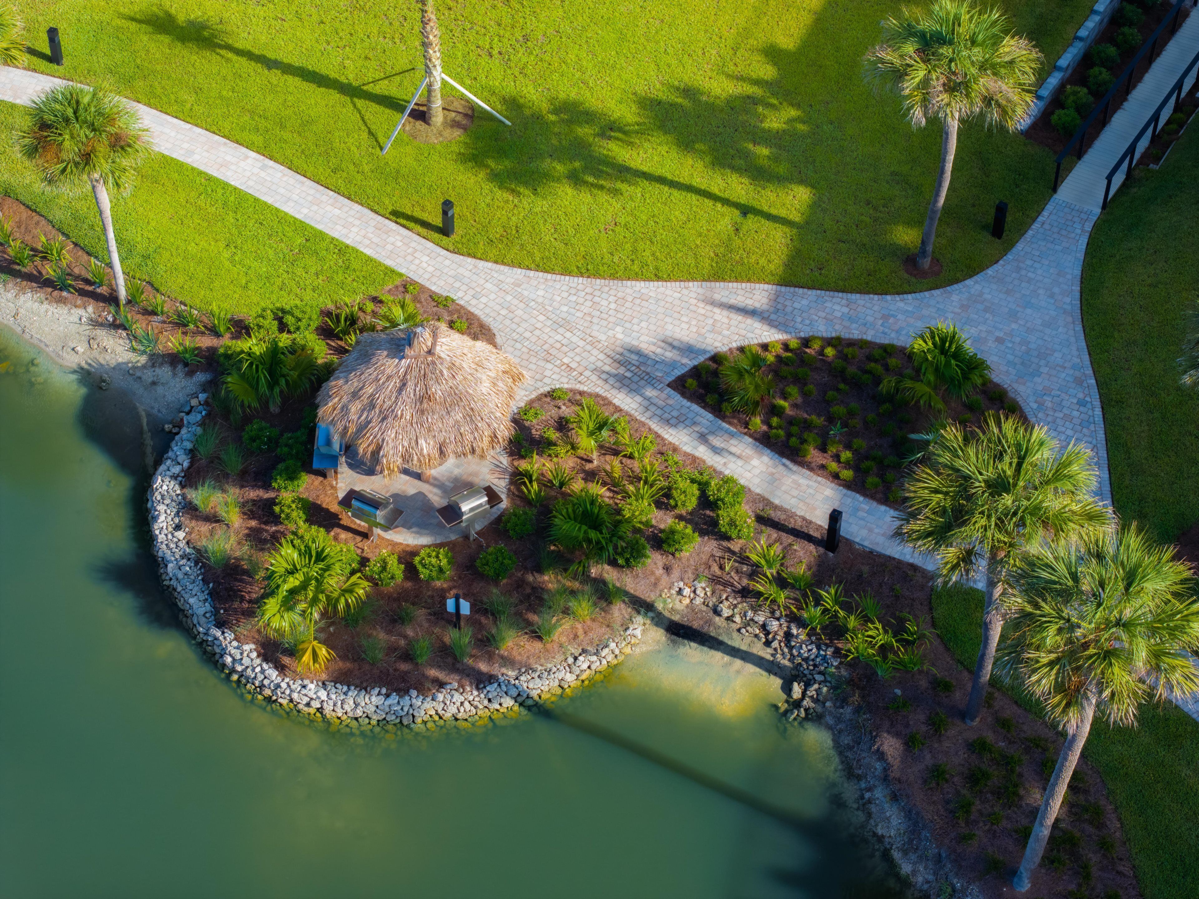 An aerial view of a landscaped area with a circular water feature, a thatched-roof structure, and a paved walkway.
